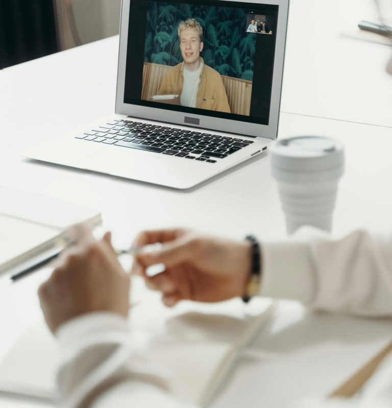 Professional virtual meeting with focus on laptop screen showing a video call participant.